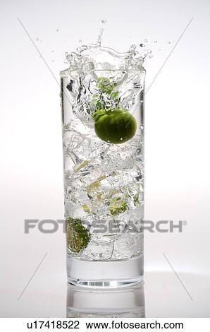 Stock Image - Kumquats dropping into a glass of water, splashing water out of the glass. Fotosearch