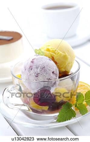 Stock Image - Taro and mango ice cream scoops in a teacup, with fruits and garnish. Fotosearch