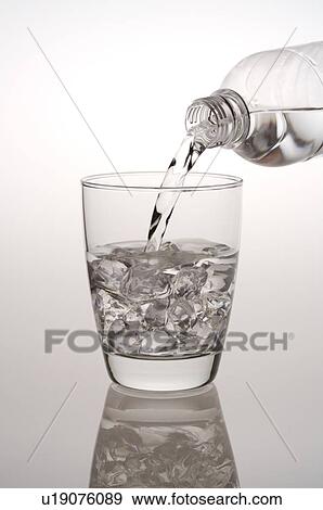 Stock Photo - Water being poured from a water bottle into a glass filled with ice cubes. Fotosearch