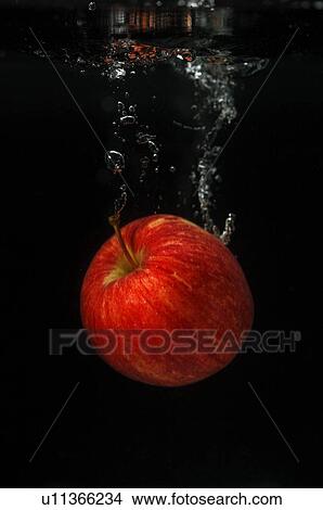 Picture - An apple falling into water against a black background, creating water bubbles. Fotosearch