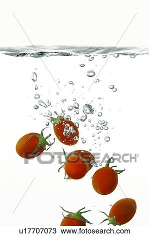 Stock Image - Cherry tomatoes falling in water, with water bubbles. Fotosearch