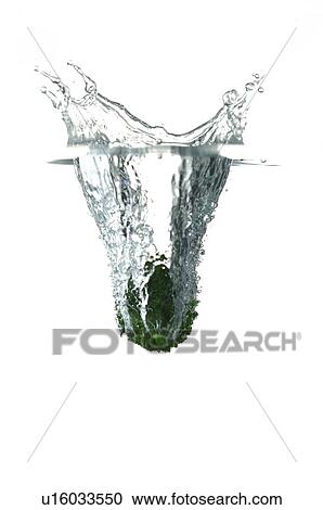 Stock Image - Green lemon falling into water, splashing water upwards. Fotosearch