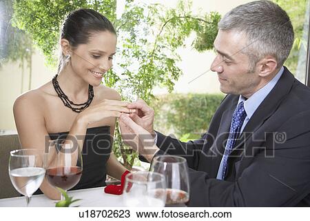 Stock Image - Man placing engagement ring on woman's finger. Fotosearch