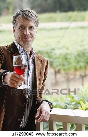 Stock Image - Mid adult man toasting with red wine (portrait). Fotosearch