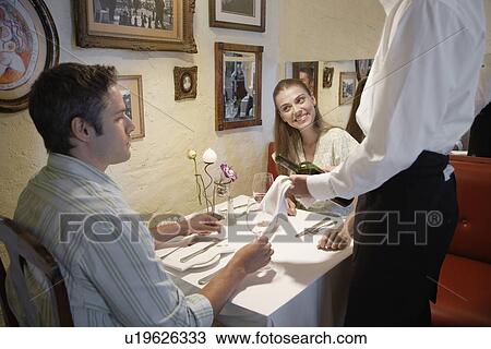 Stock Image - Waiter pouring red wine for young couple. Fotosearch