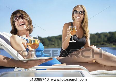Stock Image - Women having drinks on lounge chairs. Fotosearch
