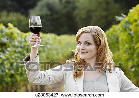 Stock Photo - Young woman holding glass of red wine in vineyard (portrait). Fotosearch