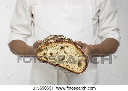 Stock Image - Chef holding loaf of bread (mid section). Fotosearch
