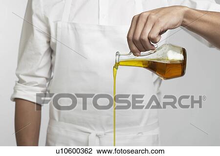 Stock Image - Chef pouring olive oil (mid section). Fotosearch