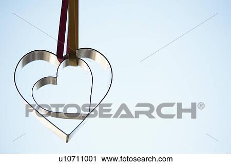 Stock Image - Two heart shaped cookie cutters hanging (close-up). Fotosearch