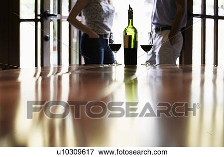 Couple standing near bottle of red wine (focus on foreground) View Large Photo Image Stock Photo - Couple standing near bottle of red wine (focus on foreground). Fotosearch