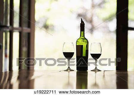Stock Image - Two glasses of red wine and bottle on table. Fotosearch