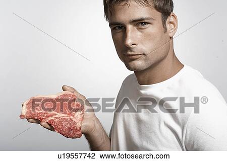 Stock Image - Mid adult man holding steak. Fotosearch