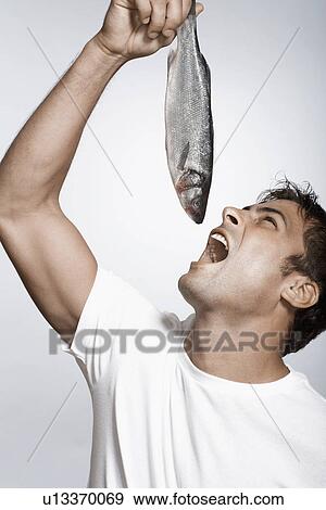 Stock Photo - Mid adult man holding striped sea bass above his mouth. Fotosearch