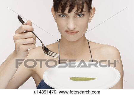 Stock Image - Mid adult woman eating single mangetout. Fotosearch