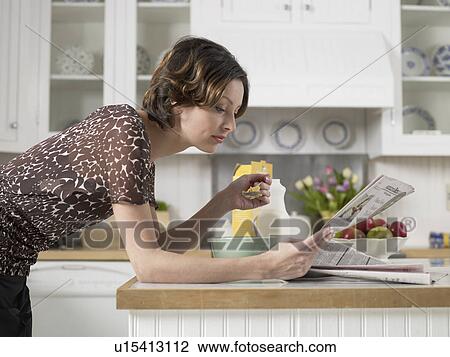 Mid adult woman reading newspaper while having breakfast at kitchen counter View Large Photo Image Stock Image - Mid adult woman reading newspaper while having breakfast at kitchen counter. Fotosearch