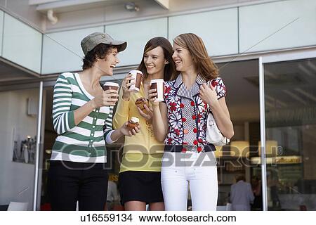 Picture - Three teenage girls drinking take-out coffees and eating cakes. Fotosearch