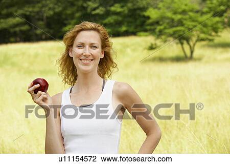 Stock Image - Woman eating apple in field. Fotosearch