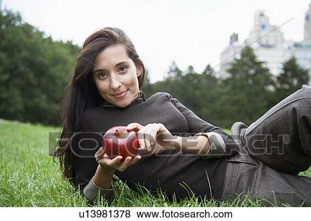 Stock Photo - Young woman eating apple on grass (portrait). Fotosearch