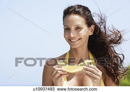 Stock Image - Young woman eating melon. Fotosearch