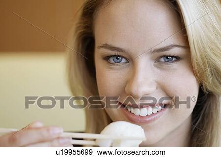 Stock Photo - Young woman eating with chopsticks. Fotosearch