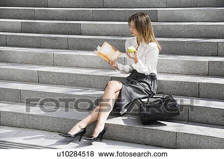 Stock Photo - Young woman reading and eating on steps. Fotosearch