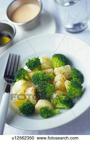 Stock Image - Broccoli and potatoes salad with fork on plate, glass and two salad dressings visible in background, Differential Focus. Fotosearch