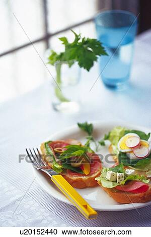 Stock Image - Mixed salad on baguette with fork, glasses and leaf visible in background, Differential Focus. Fotosearch