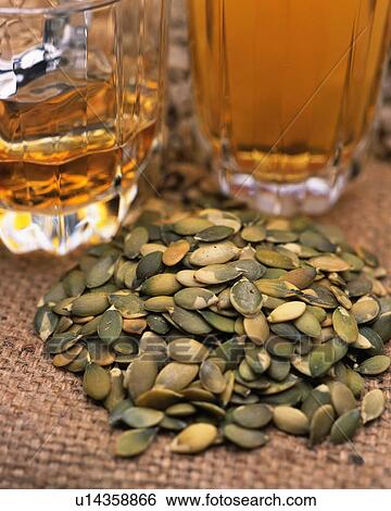 Stock Photograph - Closed Up Image of Several Pumpkin Seeds Next to Two Glasses of Beer, High Angle View, Differential Focus. Fotosearch