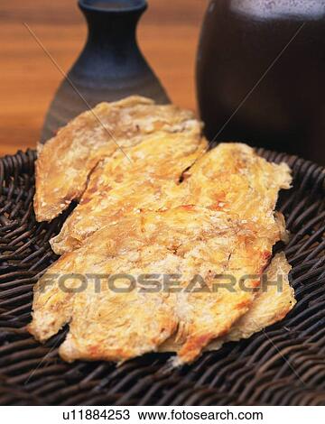 Stock Image - Closed Up Image of Some Dried Blowfish on a Wooden Plate, Next to a Bottle of Sake. Fotosearch