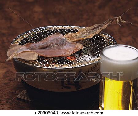 Stock Image - Closed Up Image of Some Fish Being Grilled on a Japanese Grill and Some Beer, High Angle View. Fotosearch