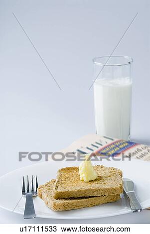 Stock Image - Close-up of a glass of milk near a newspaper and breakfast in a plate. Fotosearch
