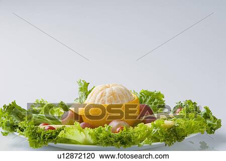 Stock Image - Close-up of a peeled orange with lettuce and baby corn on a plate. Fotosearch
