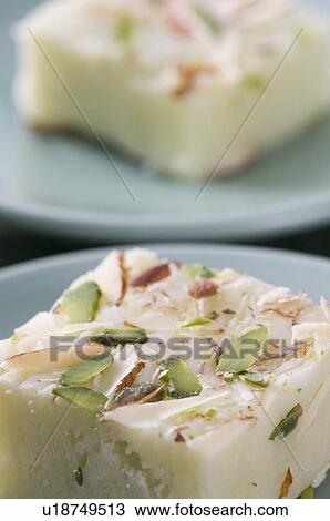 Stock Image - Close-up of Burfi garnished with Almond and Pistachio in a saucer. Fotosearch