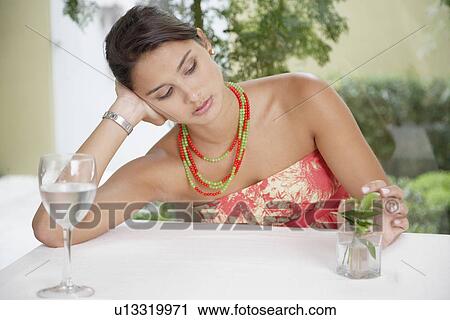 Stock Image - Bored woman playing with plant at dining table. Fotosearch