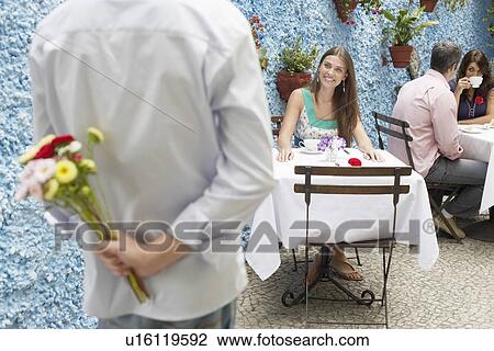 Man holding bunch of flowers behind his back, woman waiting at table View Large Photo Image Stock Image - Man holding bunch of flowers behind his back, woman waiting at table. Fotosearch