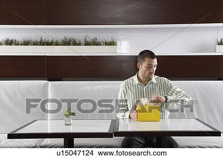 Man with present checking the time in restaurant View Large Photo Image Picture - Man with present checking the time in restaurant. Fotosearch