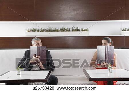 Stock Photo - Woman and man with menus over their face looking at each other. Fotosearch