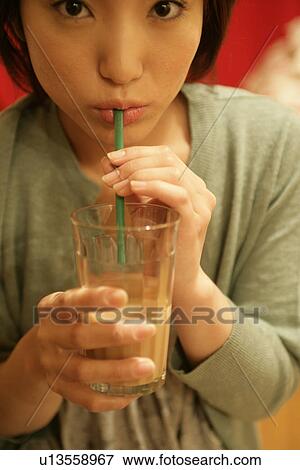 Close up of a young woman taking a sip from a glass as she stares at the camera View Large Photo Image Stock Photo - Close up of a young woman taking a sip from a glass as she stares at the camera. Fotosearch
