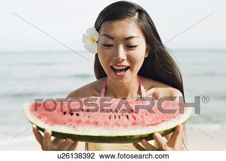 Stock Image - View of a young woman eating watermelon. Fotosearch
