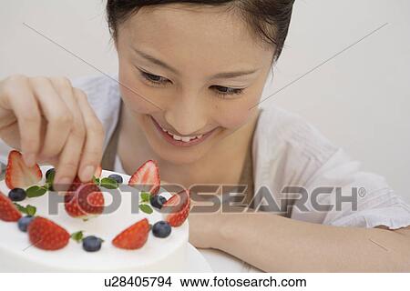 Picture - View of a young woman garnishing a pastry. Fotosearch