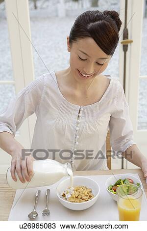 Stock Image - View of a young woman pouring milk in a bowl. Fotosearch