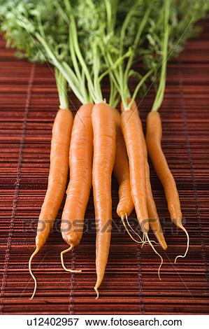 Stock Photo - Close up of orange carrots with green tops against bamboo mat.. Fotosearch