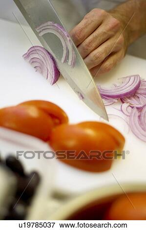 Stock Photo - Detail of hand chopping red onion with sliced tomatoes in foreground. Fotosearch