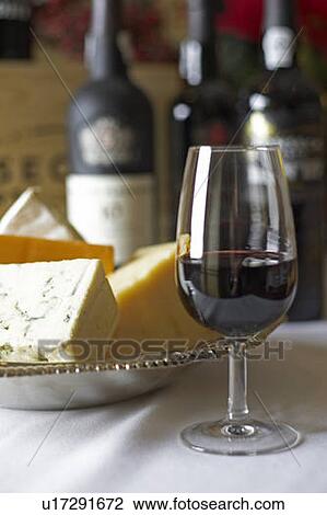 Stock Image - Glass of red wine with bricks of blue, cheddar, parmesan, and brie cheese in a silver dish. Fotosearch