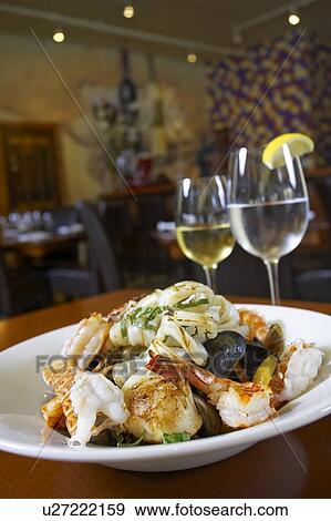 Stock Photo - Seafood dish with white wine and glass of water in restaurant setting. Fotosearch