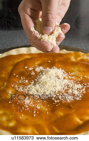 Stock Image - Man sprinkling cheese on pizza. Fotosearch