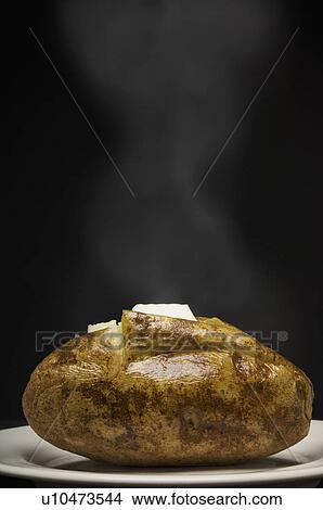 Picture - Steaming baked potato with butter. Fotosearch