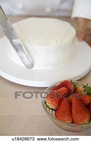 Stock Image - A woman decorating a cake with whipped cream. Fotosearch