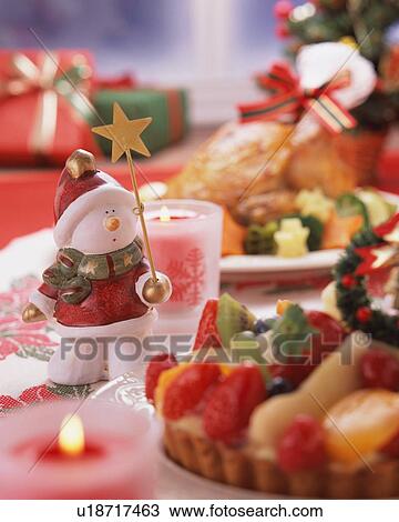 Stock Image - Statuette of a snowman holding a magic wand on table with Christmas dinner. Fotosearch